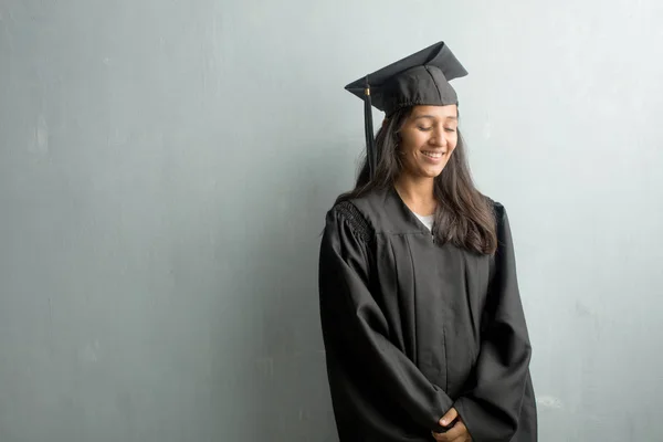 Young graduated indian woman against a wall laughing and having fun, being relaxed and cheerful, feels confident and successful