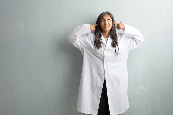 Young indian doctor woman against wall covering ears with hands