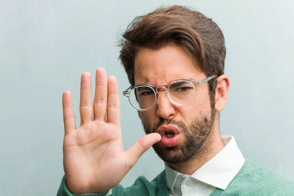 Young handsome entrepreneur man face closeup serious and determined, putting hand in front, stop gesture, deny concept