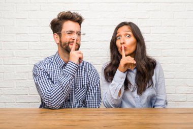 Young indian woman and caucasian man couple keeping a secret or asking for silence, serious face, obedience concept clipart