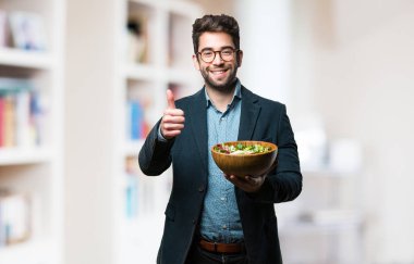 Genç adam bir salata tutan iyi jest yapıyor kase üzerinde arka plan bulanık