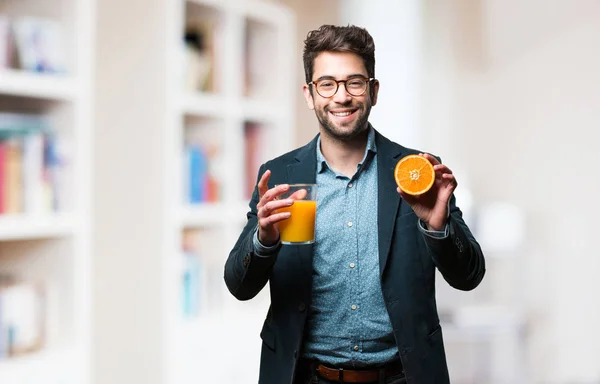 young man holding a glass of juice and an orange on blurred background