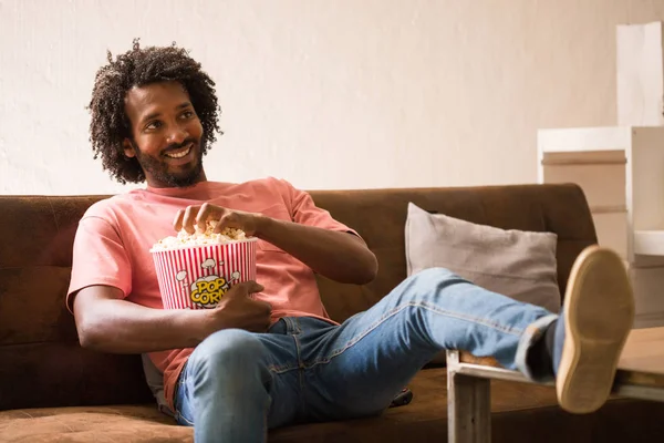 Young african man watching a movie holding a popcorn bucket.