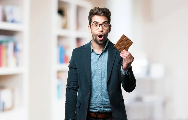 Surprised Young Man Holding Chocolate Bar Blurred Background — Stock Photo, Image