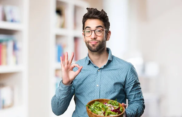 Joven Sosteniendo Una Ensalada Haciendo Buen Gesto Sobre Fondo Borroso — Foto de Stock