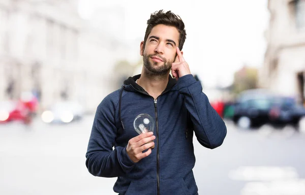 Young Man Holding Light Bulb Thinking Blurred Background — Stock Photo, Image