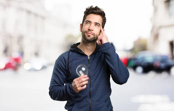 Giovane Possesso Una Lampadina Pensando Sfondo Sfocato — Foto Stock