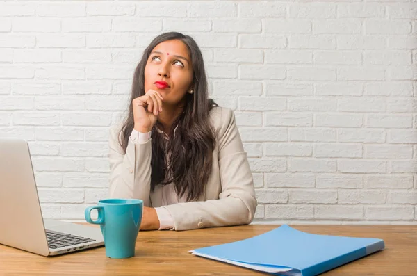 Young indian woman at office doubting and confused, thinking of idea or worried about something