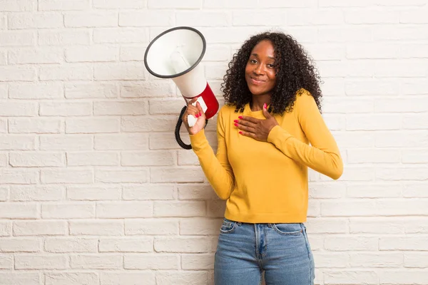 Young black woman with megaphone doing a romantic gesture against brick wall