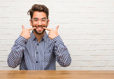 Ağız, mükemmel dişler, beyaz dişler, kavramı işaret gülümsüyor, oturan genç beyaz adam neşeli ve neşeli bir tutum vardır