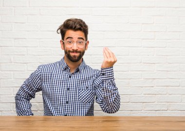 Tipik bir İtalyan jest yapıyor, gülümseyen ve dümdüz bakarak, sembol veya el, çok doğal bir ifadeyle oturan genç beyaz adam