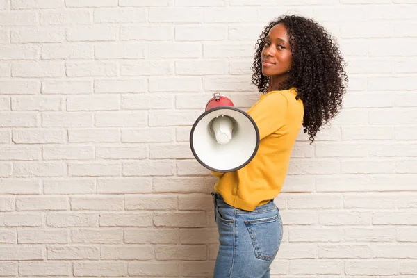 Young black woman with megaphone crossing arms against brick wall