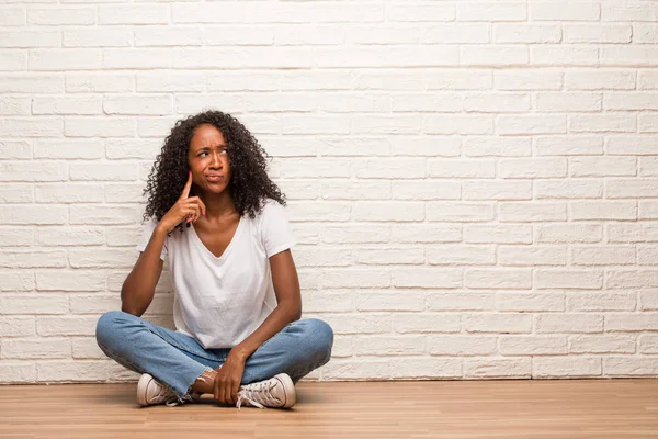 Young Black Woman Sitting Wooden Floor Doubting Confused Brick Wall — Stock Photo, Image