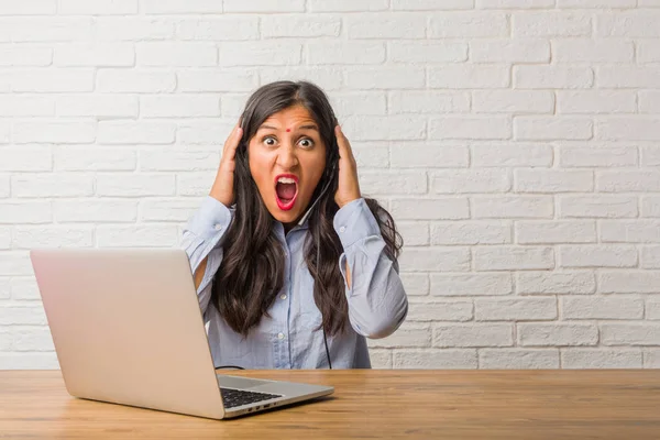 Young indian woman frustrated and desperate, angry and sad with hands on head. Wearing a headset.