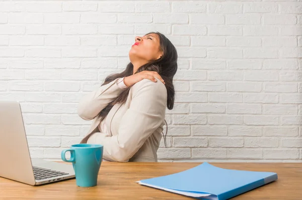 Young indian woman at office with back pain due to work stress, tired and astute