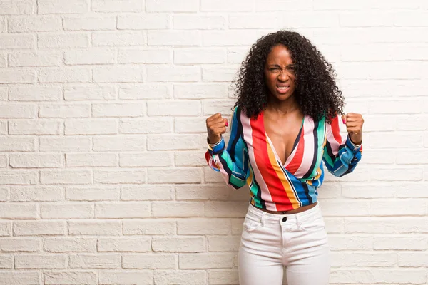 Young black woman in colorful shirt very angry and upset against brick wall