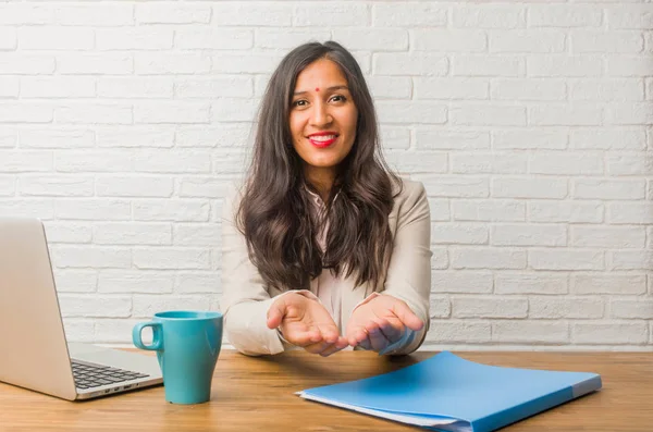 Młoda Kobieta Indyjska Biurze Trzyma Coś Rękami Wyświetlono Produktu Uśmiechnięty — Zdjęcie stockowe