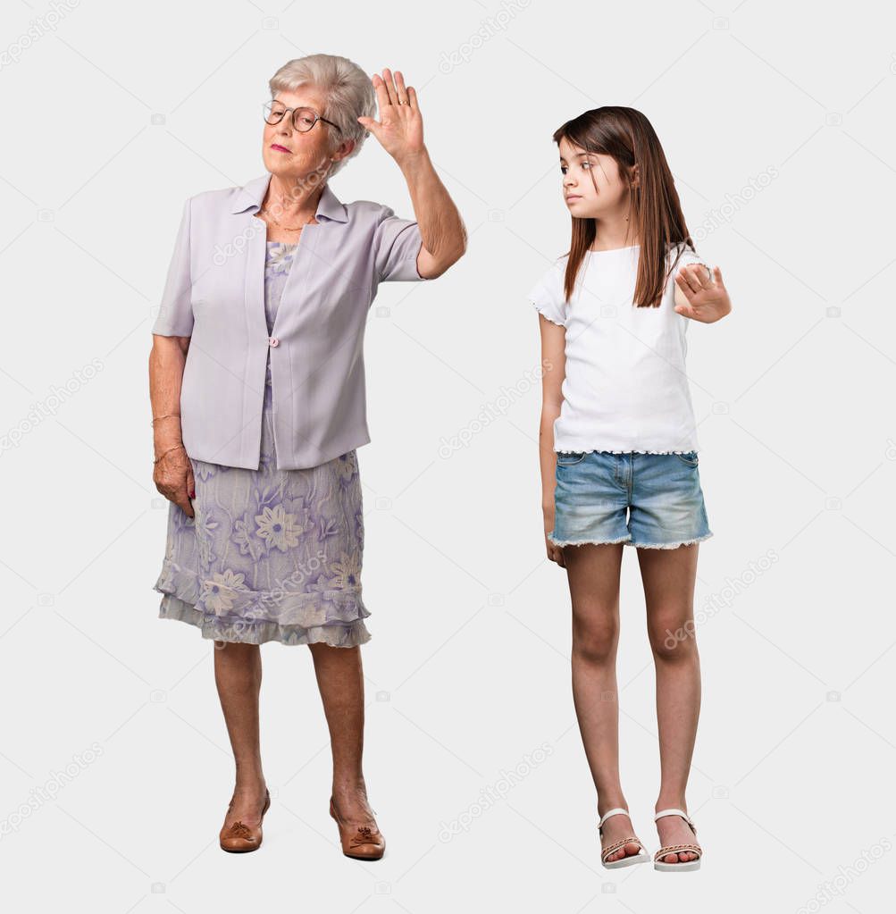 Full body of an elderly lady and her granddaughter serious and determined, putting hand in front, stop gesture, deny concept