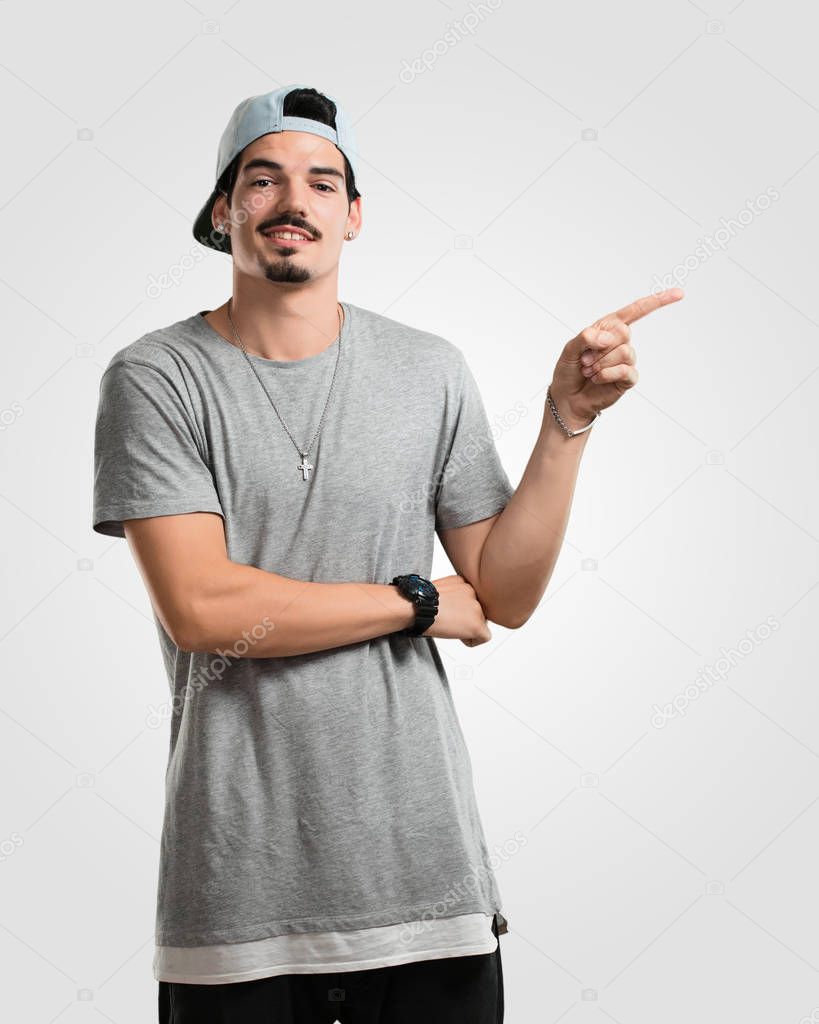 Young rapper man pointing to the side, smiling surprised presenting something, natural and casual
