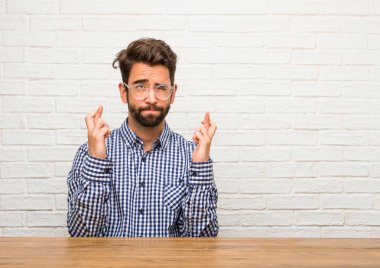 Oturan genç beyaz adam şanslı gelecekteki projelerde, gözleri kapanış endişeli, gergin ifade heyecanlı olmak istediği onun parmak kapısı