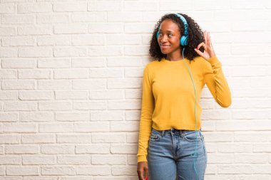 Genç siyah kadın neşeli ve kendine güvenen tuğla duvara ok jest yapıyor