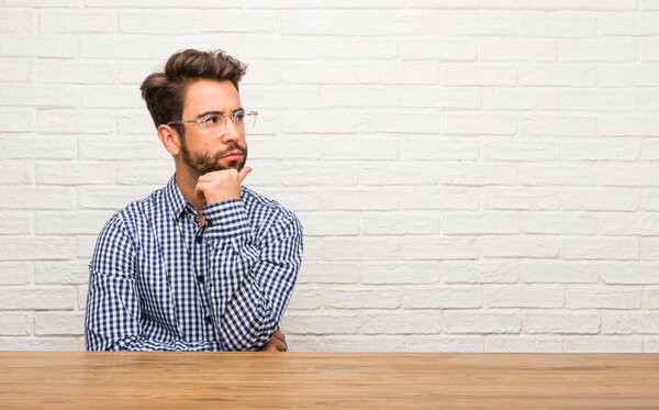 Young caucasian man sitting doubting and confused, thinking of an idea or worried about something
