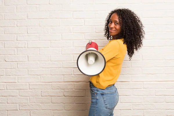 Young black woman with megaphone crossing arms against brick wall