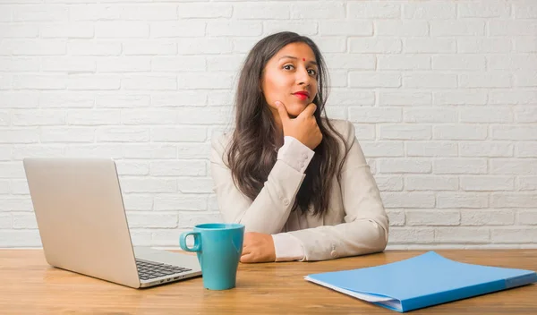 Young indian woman at the office thinking and looking up, confused about an idea, would be trying to find a solution