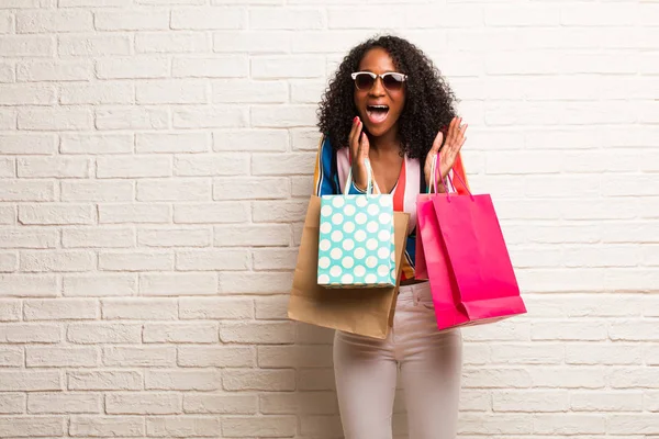 年轻的黑人妇女与购物袋笑和有乐趣反对砖墙 — 图库照片