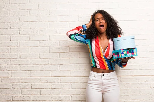 Young black woman in colorful shirt with boxes crazy and desperate against brick wall