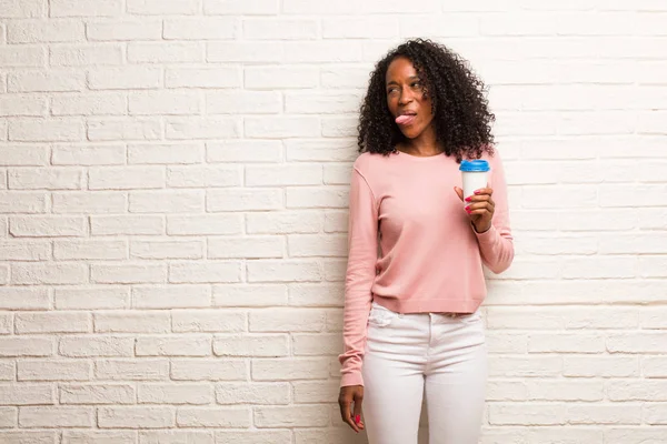 レンガの壁に舌を示す使い捨てのコーヒー カップの若い黒人女性 — ストック写真