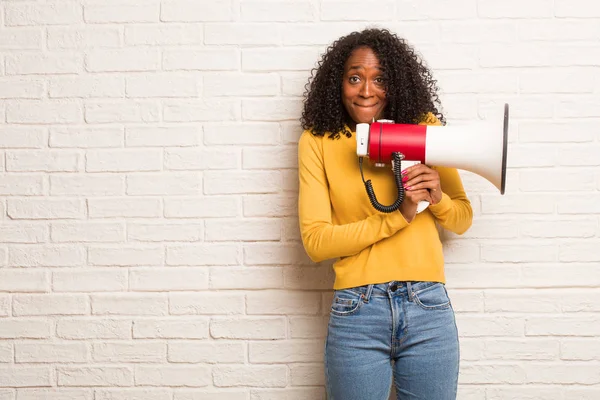 Young black woman with megaphone doubting and confused against brick wall