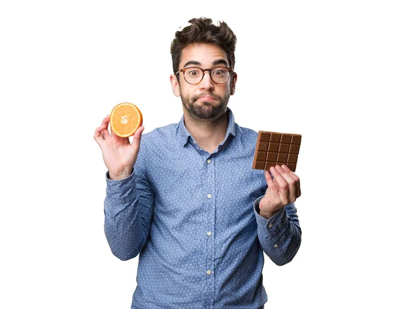 Νεαρός Άνδρας Κρατά Ένα Πορτοκάλι Και Μια Σοκολάτα Που Απομονώνονται — Φωτογραφία Αρχείου