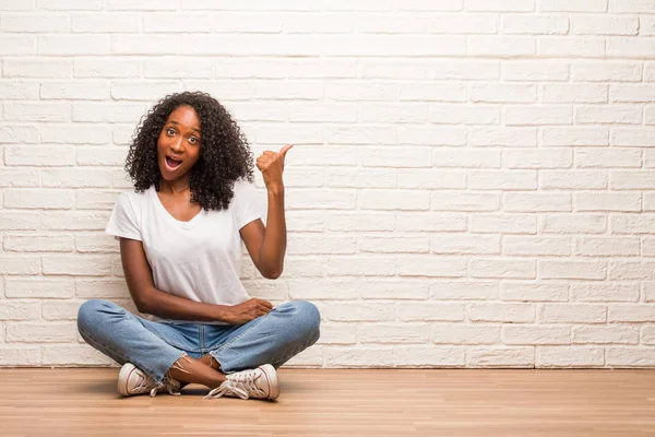 Young Black Woman Sitting Wooden Floor Pointing Side Brick Wall — Stock Photo, Image