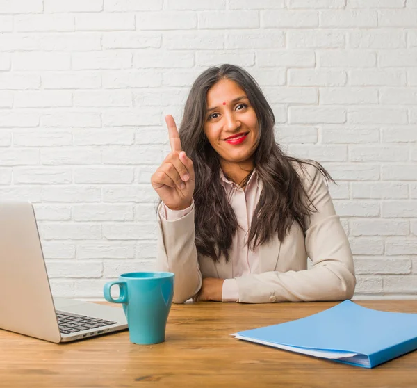 Young indian woman at the office showing number one, symbol of counting, concept of mathematics, confident and cheerful