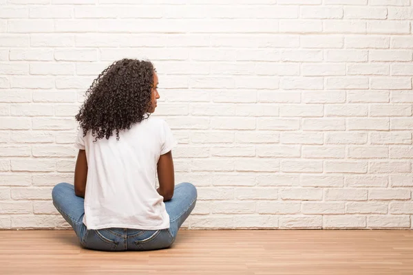 Νεαρή Μαύρη Γυναίκα Που Κάθεται Στο Ξύλινο Πάτωμα Δείχνει Πίσω — Φωτογραφία Αρχείου