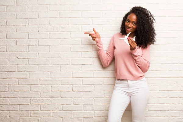 Young Black Woman Airplane Model Pointing Side Smiling Brick Wall — Stock Photo, Image