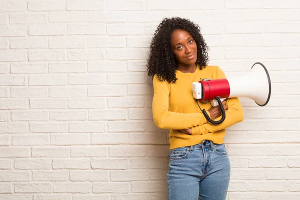 Young black woman with megaphone crossing arms against brick wall