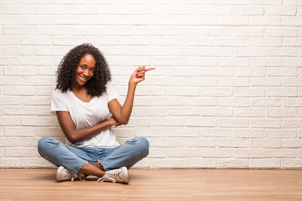 Ung Svart Kvinna Som Sitter Ett Trägolv Som Pekar Till — Stockfoto