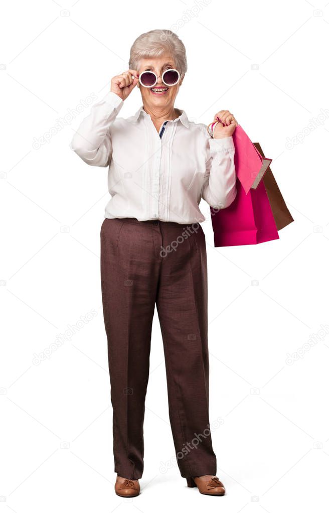 Full body senior woman cheerful and smiling, very excited carrying a shopping bags, ready to go shopping and look for new offers