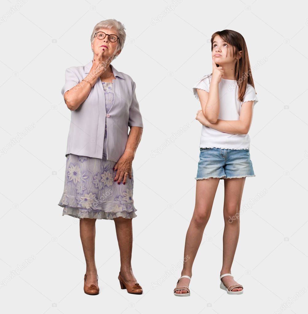 Full body of an elderly lady and her granddaughter thinking and looking up, confused about an idea, would be trying to find a solution