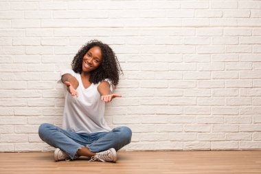 Duvara karşı selamlıyorum uzanarak bir ahşap zemin üzerinde oturan genç siyah kadın