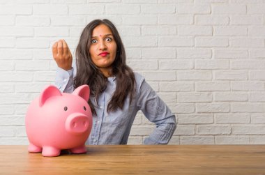 Genç Hintli kadın tipik İtalyan jest, gülümseyen ve düz ileriye baktığımızda, simge veya el, çok doğal bir ifadeyle yapıyor. Bir kumbara holding.