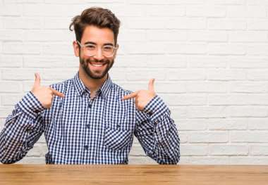 İşaret parmakları, örnek takip etmek, memnuniyeti, kibir ve sağlık kavramı gurur ve kendinden emin, oturan genç beyaz adam