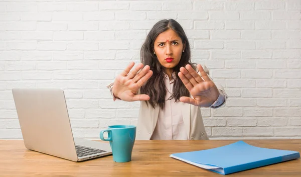 Young indian woman at the office serious and determined, putting hand in front, stop gesture, deny concept