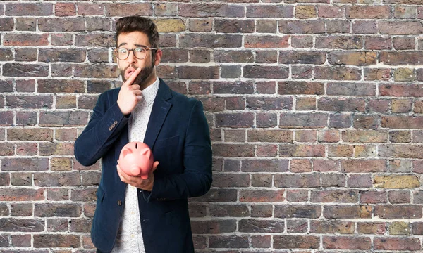 young man worried about piggy bank against brick wall