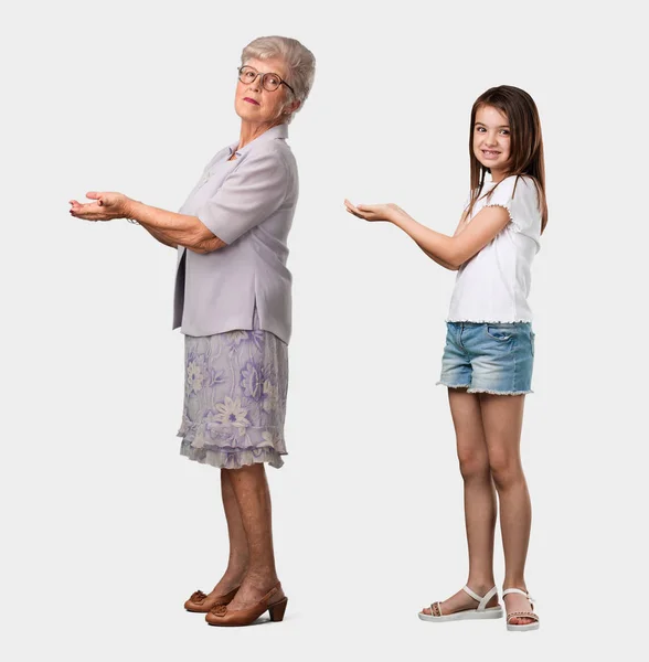 老婦人の孫娘の手で何かを保持 笑顔と陽気な製品を示し 想像上のオブジェクトを提供している完全なボディ — ストック写真