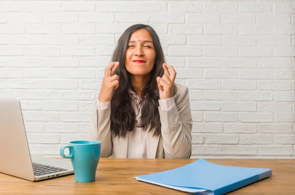 Young indian woman at office crossing fingers, wishes to be lucky for future projects