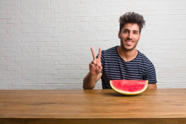 Gösterilen iki numaralı sayma simgesi, kavramı matematik, kendinden emin ve neşeli bir masada oturan genç yakışıklı ve doğal adam. Bir karpuz yeme.
