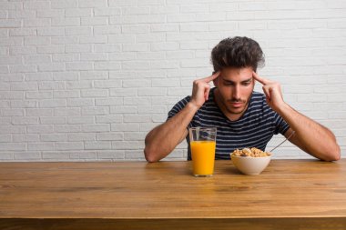 Dümdüz bir konsantrasyon jest yapma adam arayan bir tablo üzerinde oturan genç yakışıklı ve doğal adam bir hedef odaklı. Bir kahvaltı yapıyor, portakal suyu ve tahıl bowl içerir.